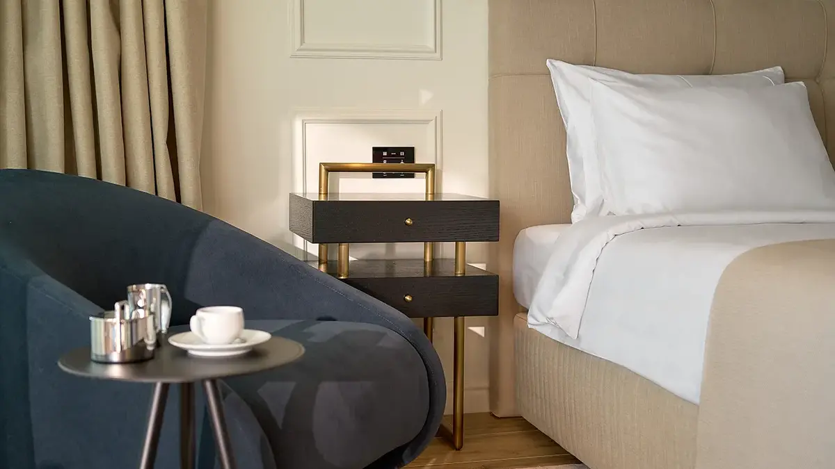 Corner of a hotel bed, with coffee and sugar on the table