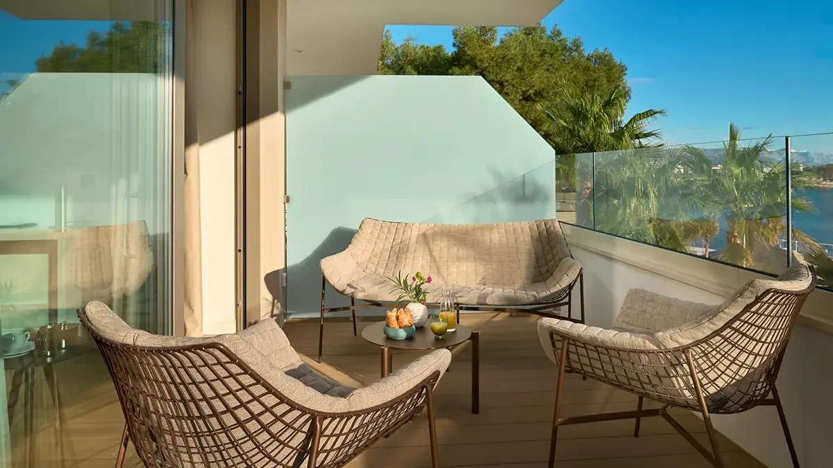 Balcony with chairs and croissants on the table, with partial sea view.
