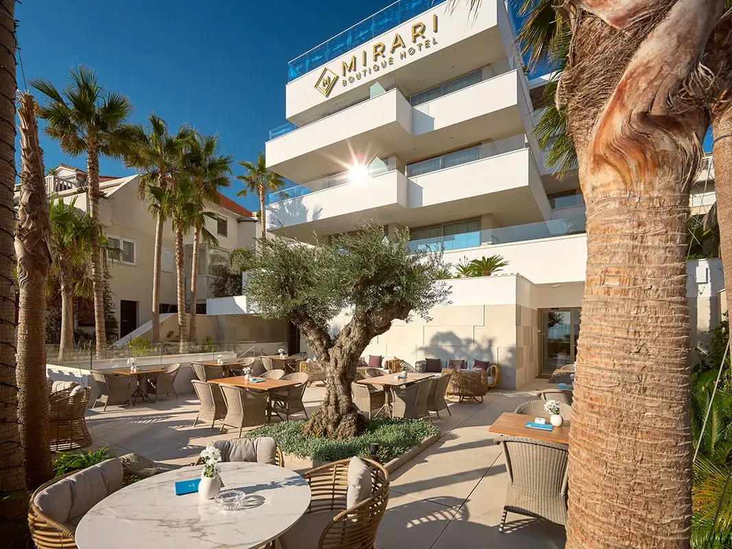 Restaurant terrace with palms, olive tree and a variety of plants in front of Boutique Hotel Mirari,